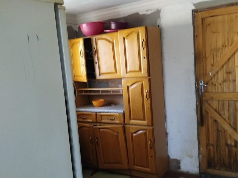 A kitchen area featuring wooden cabinetry and a wooden door, currently requiring significant renovation and finishing of the walls and flooring.