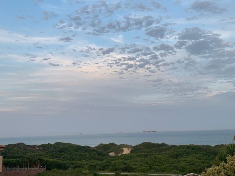 A scenic coastal view overlooking lush green dunes and the ocean horizon under a cloudy sky.