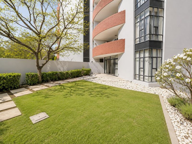 A well-maintained rear garden area featuring a manicured lawn, stone pathways, and a modern apartment building facade with curved brick balconies.