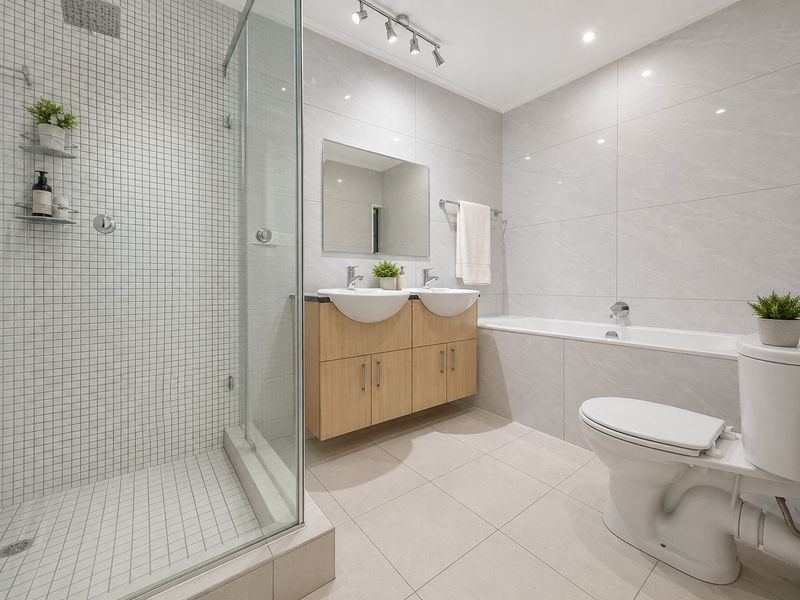 Modern bathroom featuring a double vanity, glass-enclosed shower, and a built-in bathtub with neutral tiling throughout.