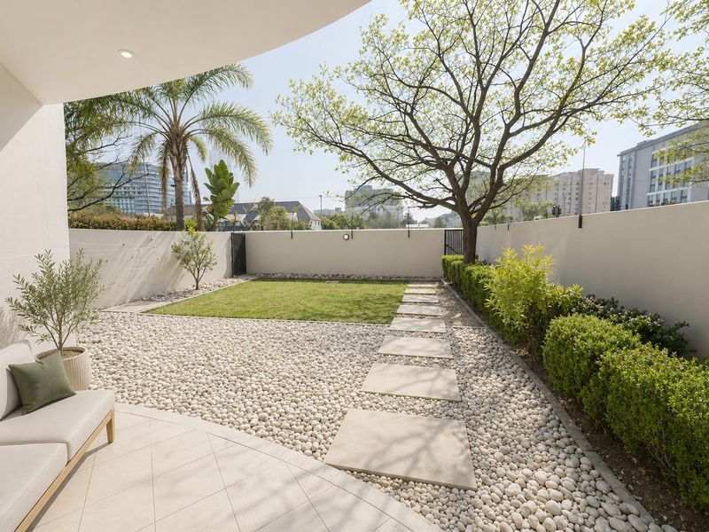 A well-maintained private rear garden featuring a tiled patio, pebble landscaping, a manicured lawn, and a stone pathway enclosed by a perimeter wall.