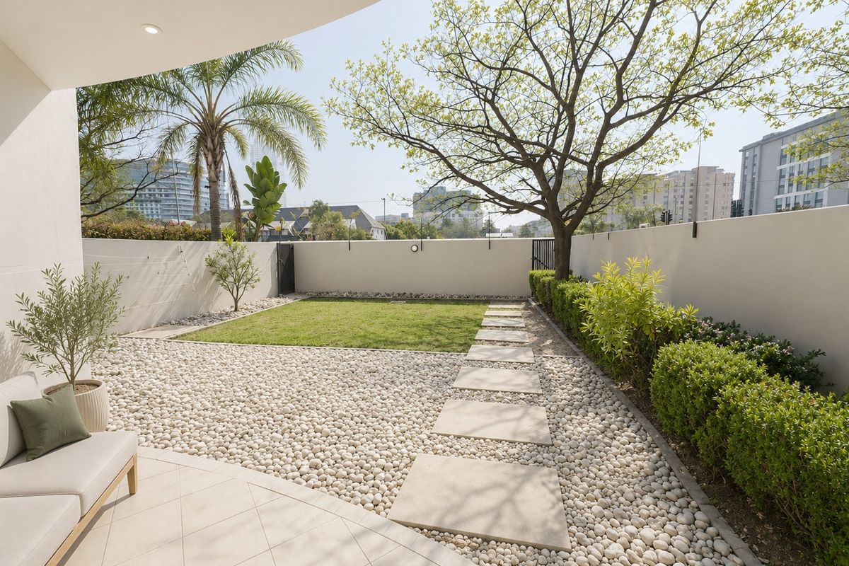 A well-maintained private rear garden featuring a tiled patio, pebble landscaping, a manicured lawn, and a stone pathway enclosed by a perimeter wall.