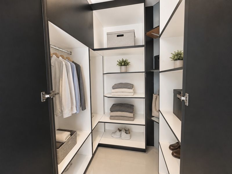 A modern walk-in wardrobe featuring custom built-in cabinetry with black frames, white shelving, and integrated hanging rails.