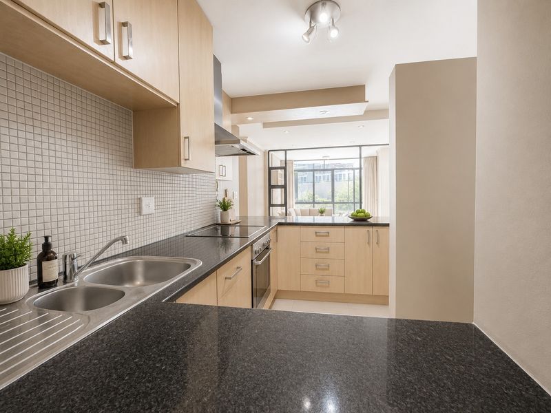 Modern kitchen featuring light wood cabinetry, dark granite countertops, mosaic tile backsplash, and integrated stainless steel appliances, flowing into an open-plan living area.