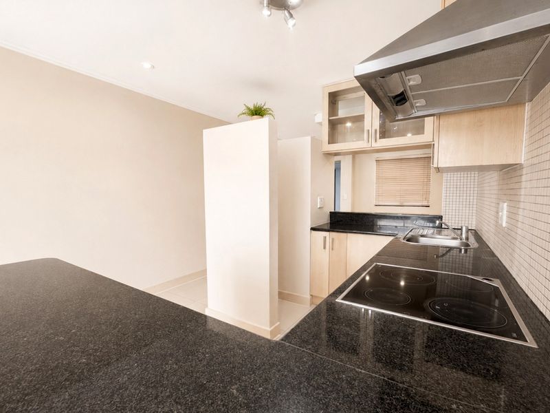 A clean, functional kitchen featuring granite countertops, a built-in electric hob with extractor fan, and ample cabinetry for storage.