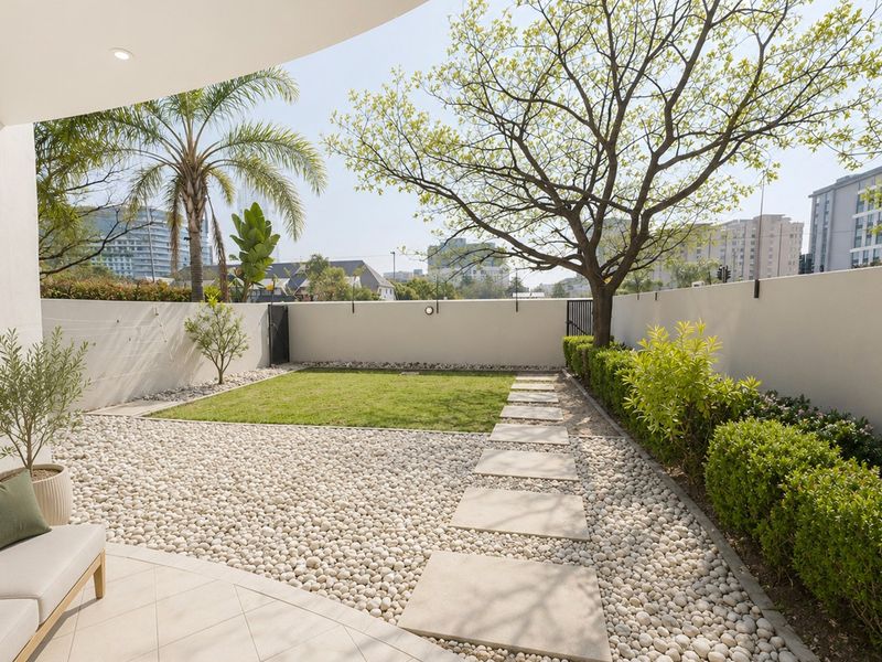 A well-maintained private rear garden featuring a paved patio, pebble landscaping, a small lawn, and a secure boundary wall.