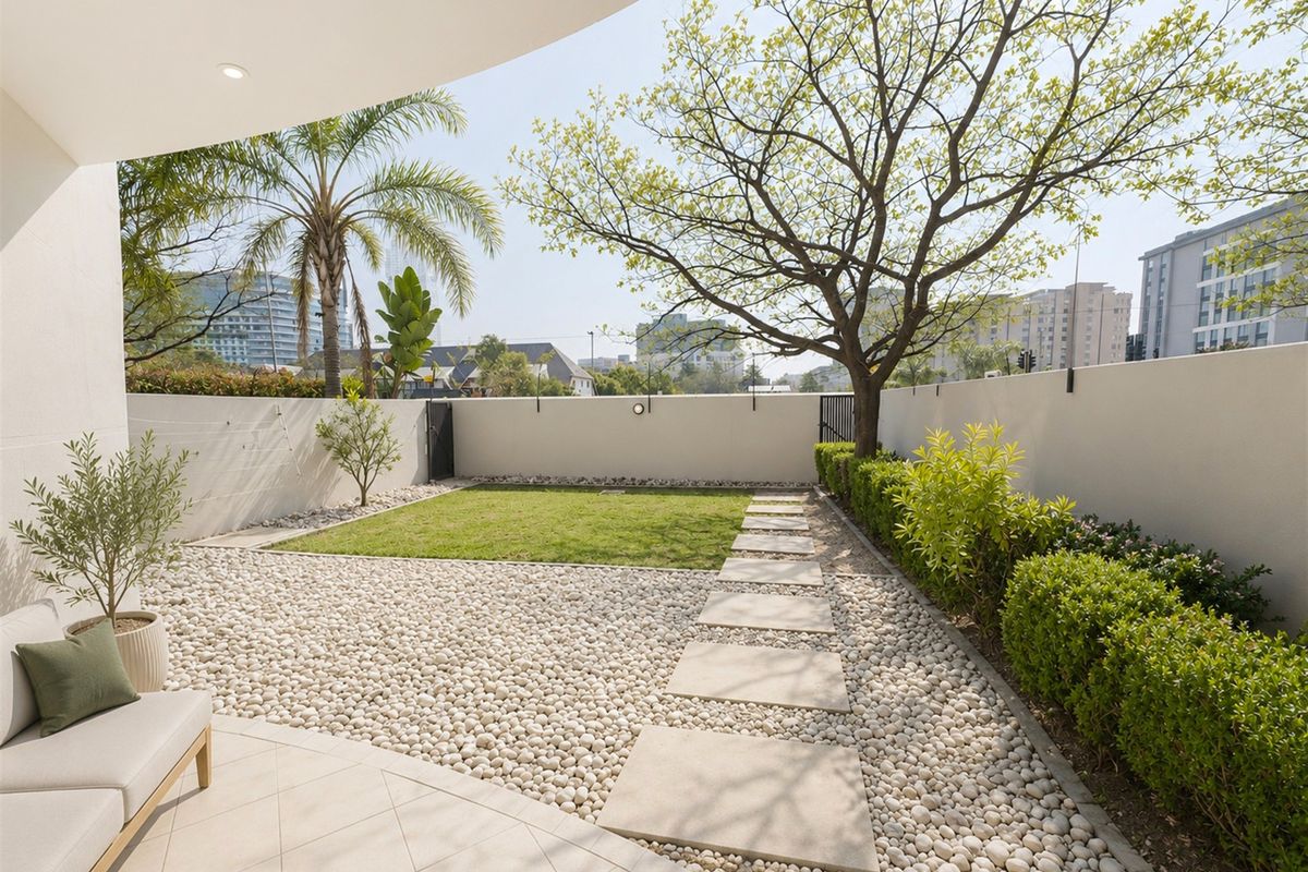 A well-maintained private rear garden featuring a paved patio, pebble landscaping, a small lawn, and a secure boundary wall.