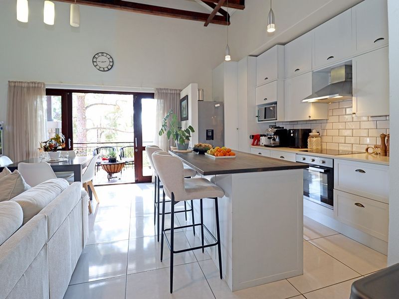 Spacious open-plan living and kitchen area featuring a central island, modern cabinetry, subway tile backsplash, and exposed timber beams leading to a balcony.