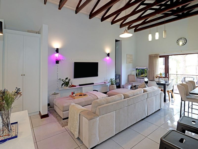 Spacious open-plan living and dining area featuring high ceilings with exposed timber rafters, tiled flooring, and direct access to an outdoor patio.