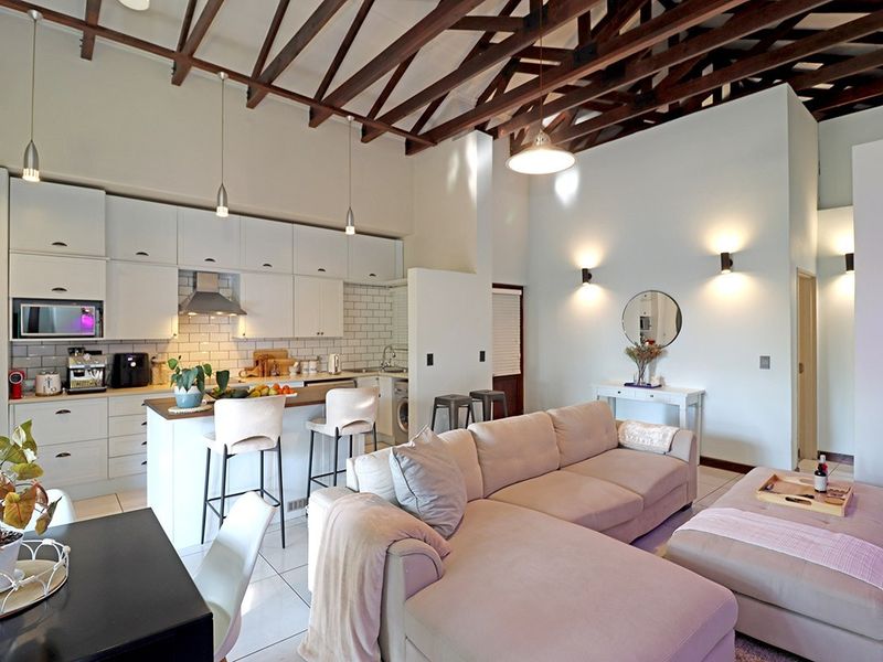 Spacious open-plan living area featuring high vaulted ceilings with exposed timber rafters, a modern kitchen with subway tile backsplash, and tiled flooring throughout.