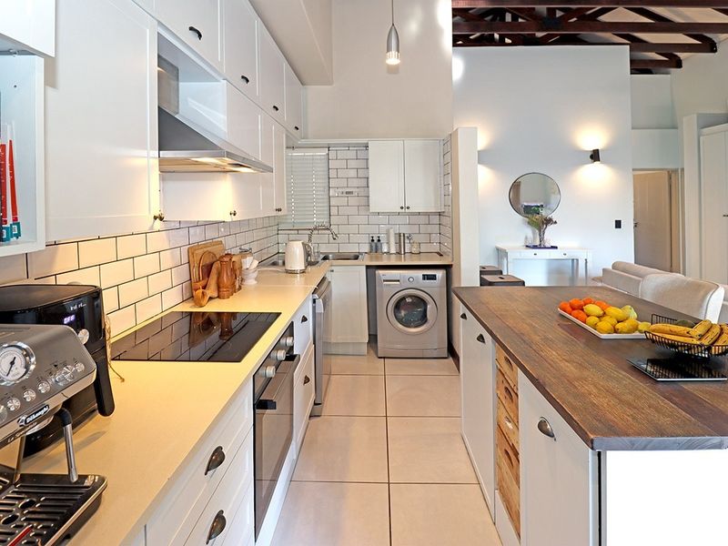 Modern kitchen featuring white cabinetry, subway tile backsplash, integrated appliances, and a timber-topped island, set under high ceilings with exposed timber beams.