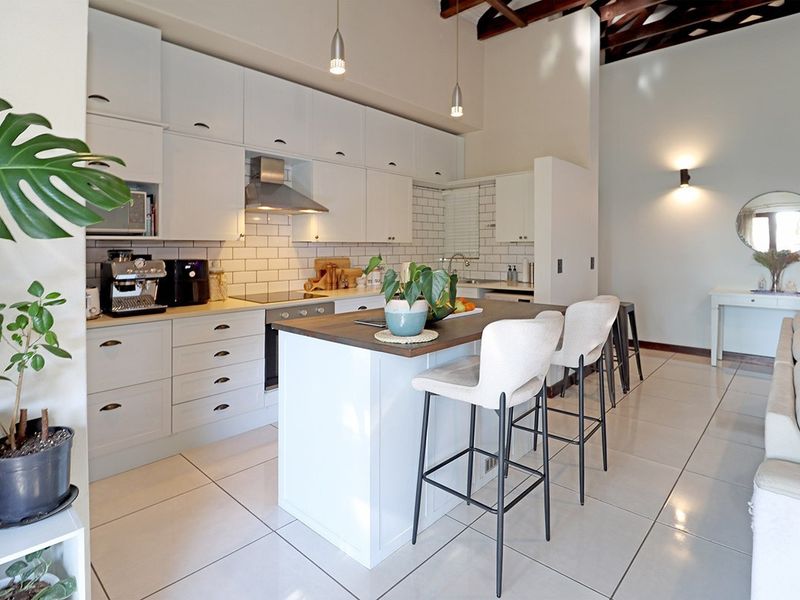 Modern open-plan kitchen featuring white cabinetry, subway tile backsplash, a central island with breakfast bar seating, and high ceilings with exposed timber beams.