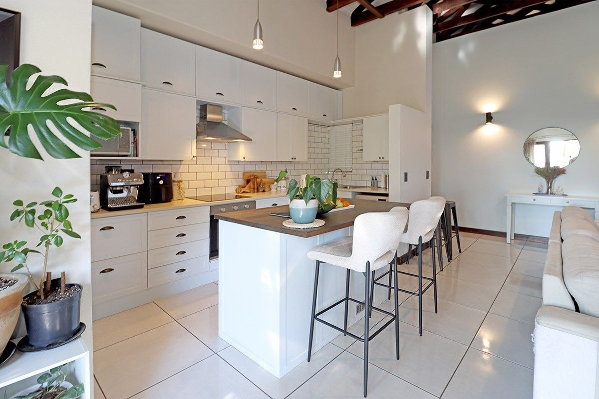 Modern open-plan kitchen featuring white cabinetry, subway tile backsplash, a central island with breakfast bar seating, and high ceilings with exposed timber beams.
