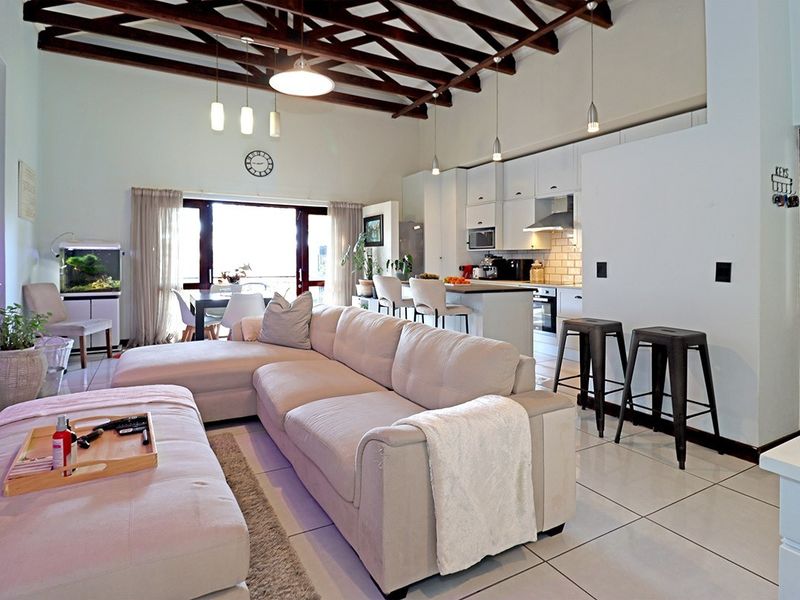 Spacious open-plan living area featuring high exposed timber beam ceilings, tiled floors, and a modern kitchen with a central island and integrated appliances.