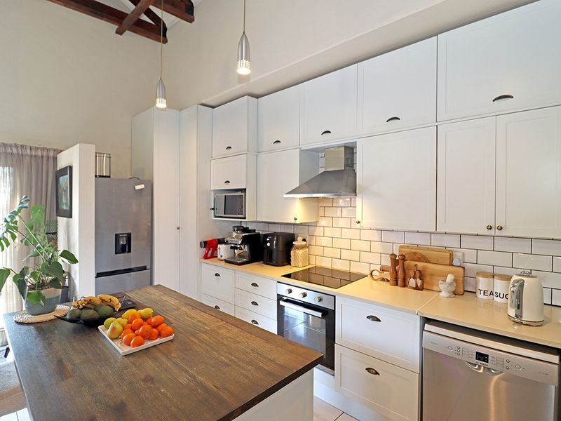 Modern kitchen featuring white cabinetry, subway tile backsplash, stone countertops, integrated appliances, and exposed timber ceiling beams.