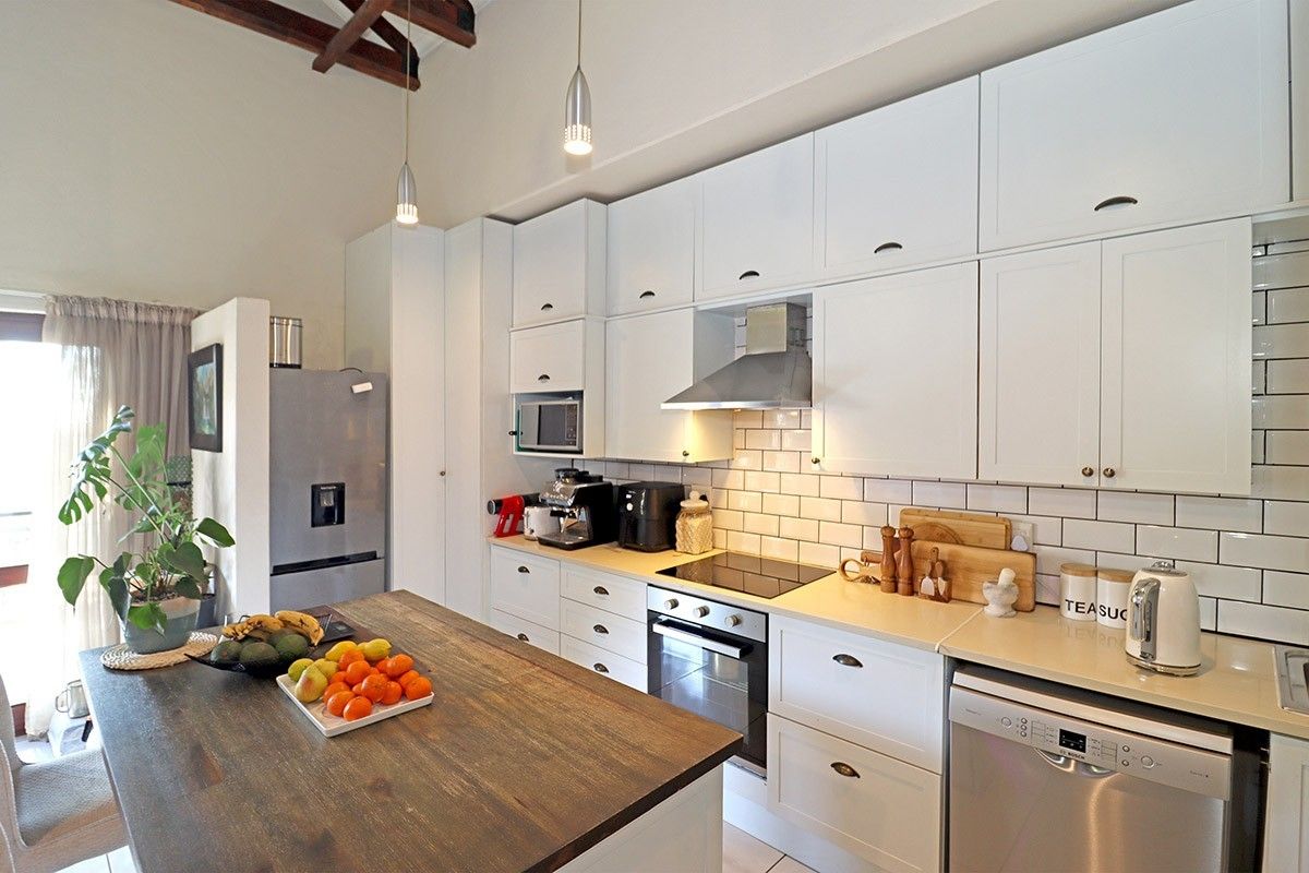 Modern kitchen featuring white cabinetry, subway tile backsplash, stone countertops, integrated appliances, and exposed timber ceiling beams.