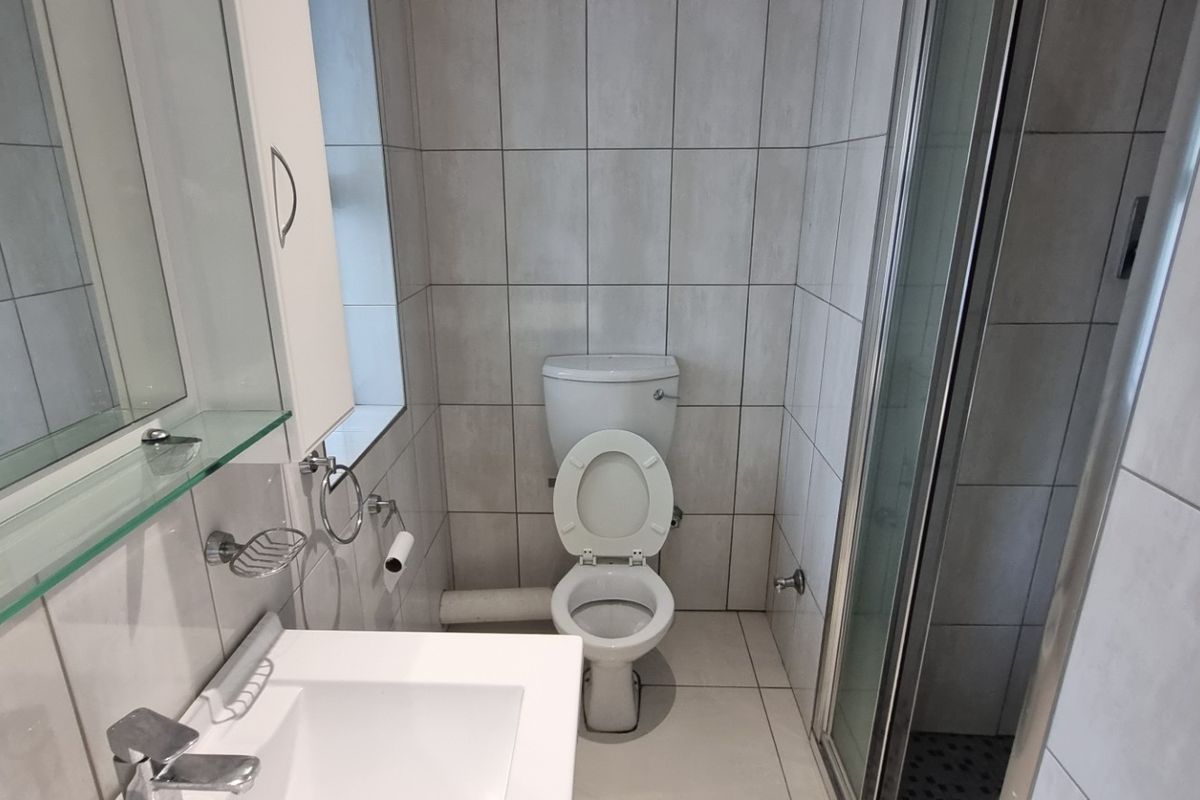 A clean, modern bathroom featuring a shower enclosure, vanity basin, and neutral wall and floor tiling.