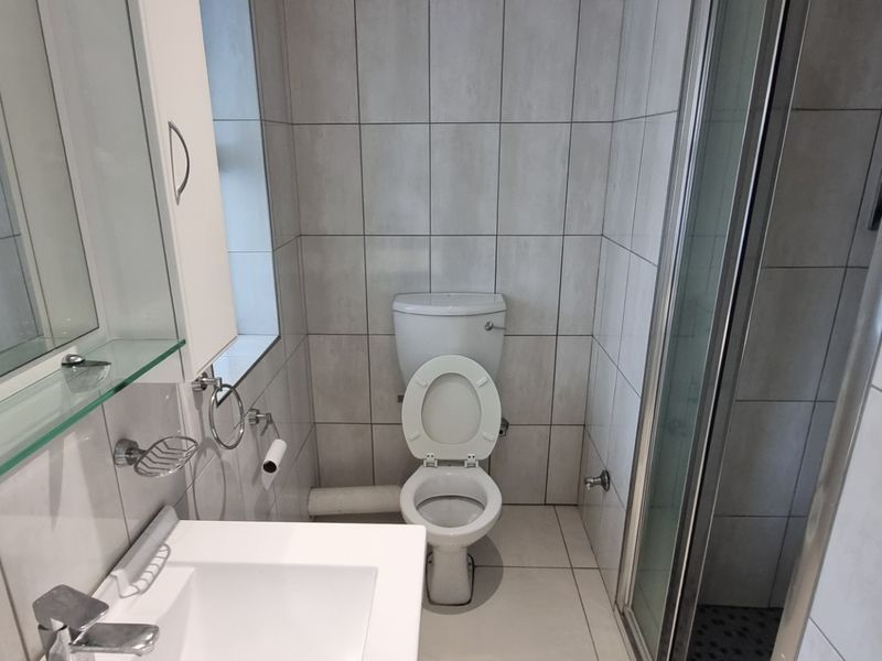A clean, modern bathroom featuring a shower enclosure, vanity basin, and neutral wall and floor tiling.