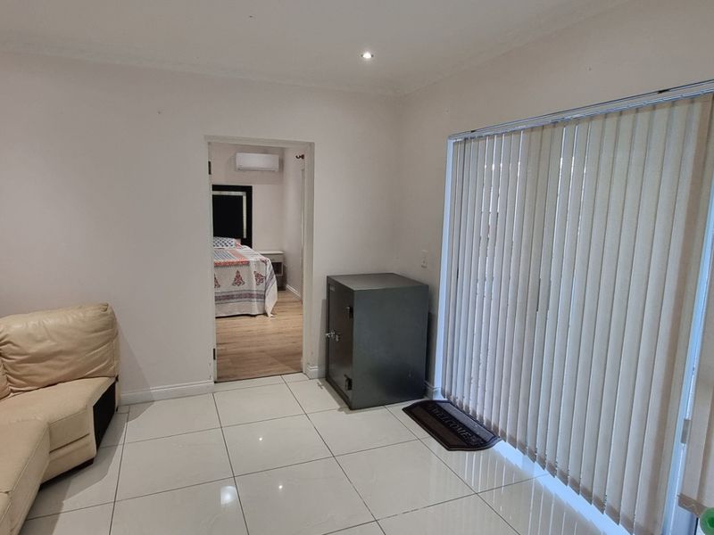 A living room featuring tiled flooring, recessed lighting, and sliding glass doors with vertical blinds, providing access to an adjacent bedroom.