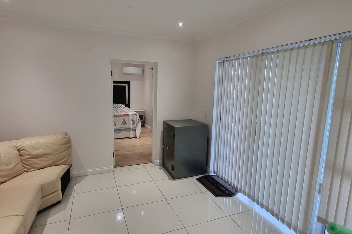 A living room featuring tiled flooring, recessed lighting, and sliding glass doors with vertical blinds, providing access to an adjacent bedroom.