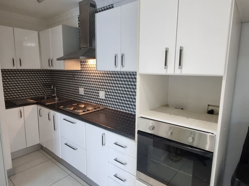 A modern, well-maintained kitchen featuring white cabinetry, a geometric tiled backsplash, stainless steel appliances, and tiled flooring.