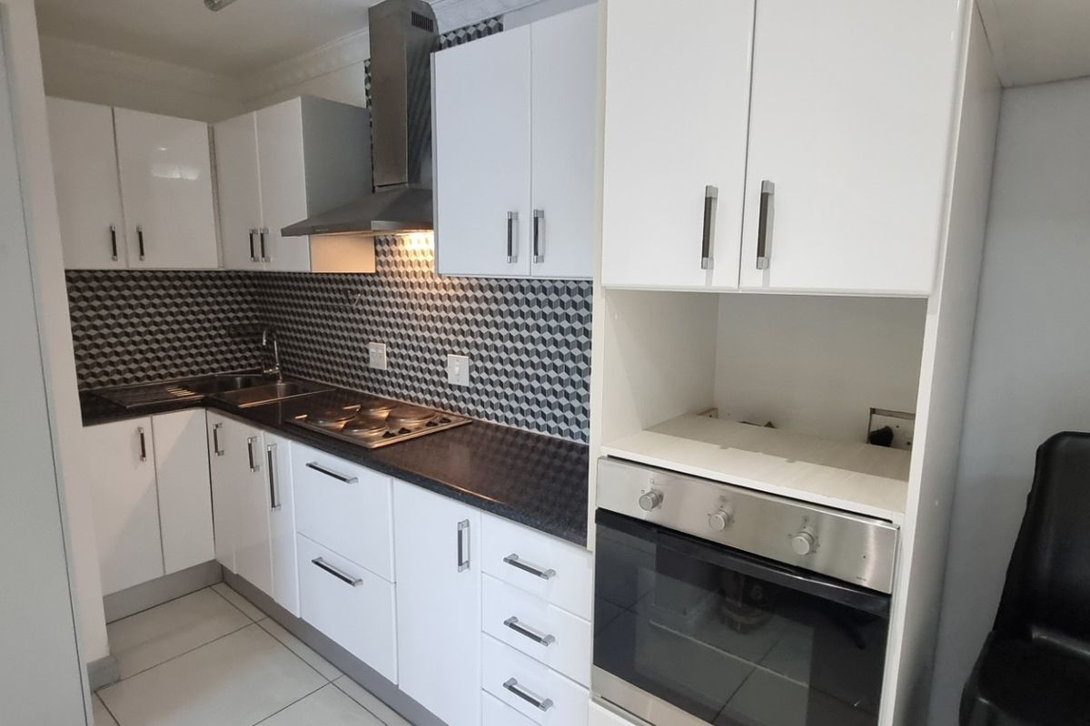 A modern, well-maintained kitchen featuring white cabinetry, a geometric tiled backsplash, stainless steel appliances, and tiled flooring.