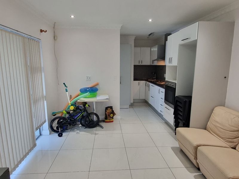 Open-plan living and kitchen area featuring tiled floors, modern white cabinetry, built-in oven, and large sliding doors with vertical blinds.
