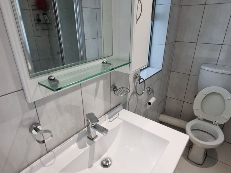 A modern bathroom featuring tiled walls and floors, a vanity basin with chrome fixtures, a toilet, and a glass-enclosed shower area.