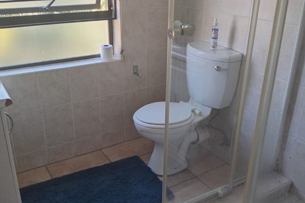 A functional bathroom featuring a shower enclosure, toilet, and neutral tiled finishes throughout.