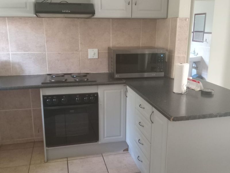 A functional kitchen featuring light grey cabinetry, dark laminate countertops, a built-in oven with electric hob, and neutral tiled flooring and backsplash.