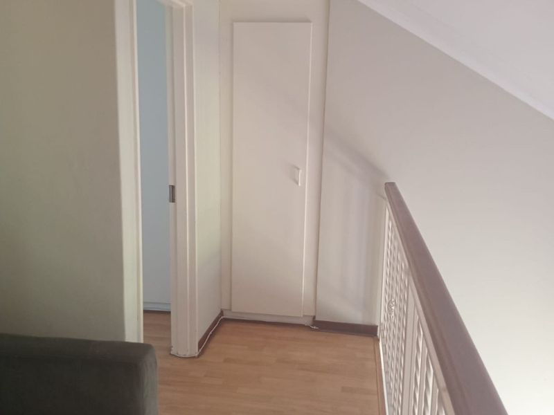 A bright upper-level hallway featuring laminate flooring, a built-in storage cupboard, and a protective railing overlooking the lower level.