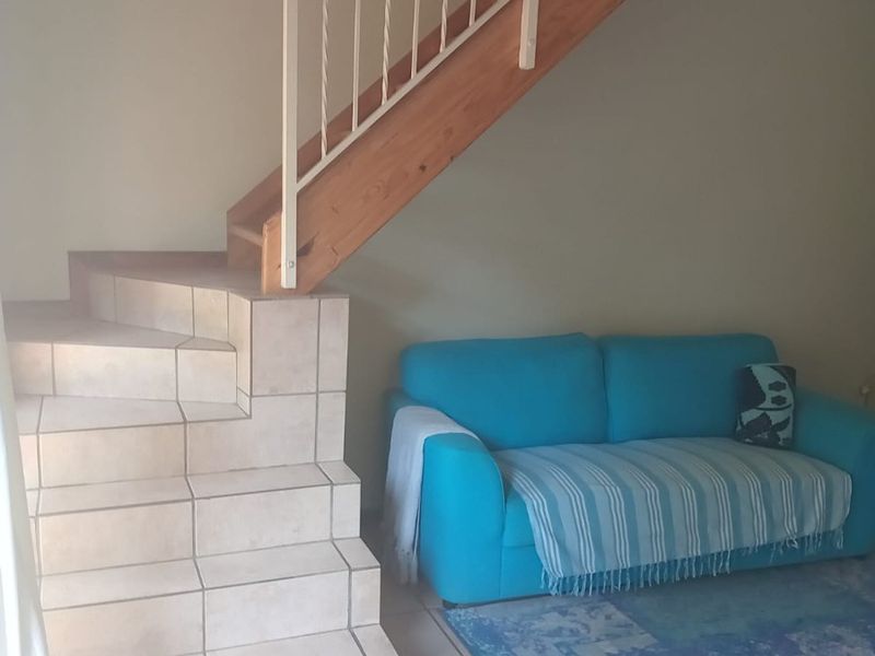 A living area featuring a unique tiled staircase with a timber stringer and metal balustrade, complemented by neutral ceramic floor tiles.