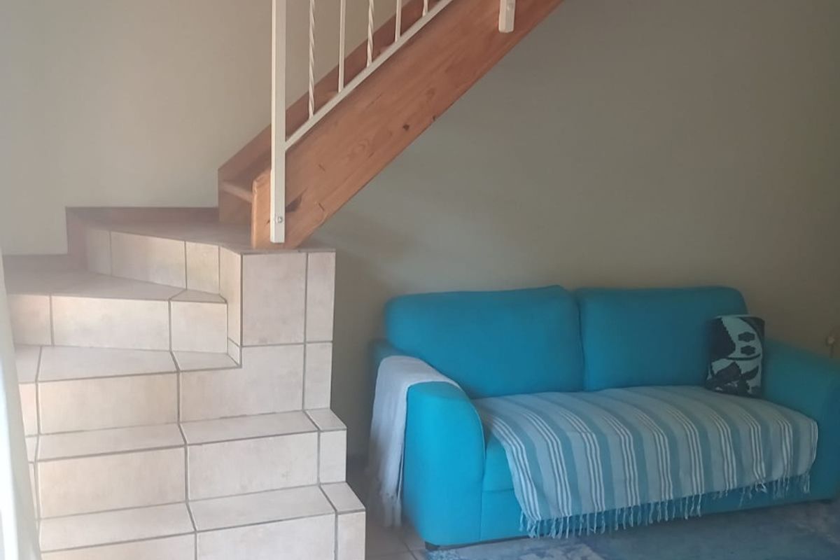 A living area featuring a unique tiled staircase with a timber stringer and metal balustrade, complemented by neutral ceramic floor tiles.
