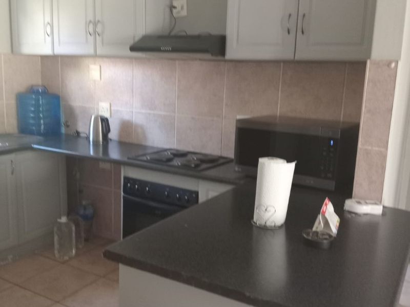 A functional kitchen featuring built-in cabinetry, dark laminate countertops, tiled backsplash, and integrated cooking appliances including an oven, hob, and extractor fan.