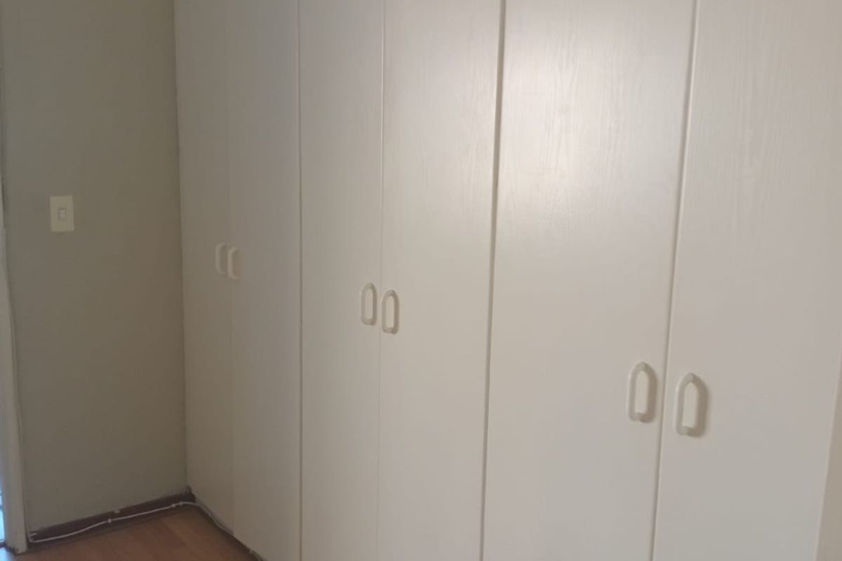 A bedroom featuring white built-in cupboards and laminate flooring, with visible surface-mounted electrical wiring along the baseboard.