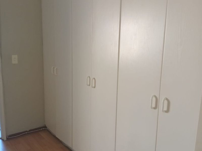 A bedroom featuring white built-in cupboards and laminate flooring, with visible surface-mounted electrical wiring along the baseboard.