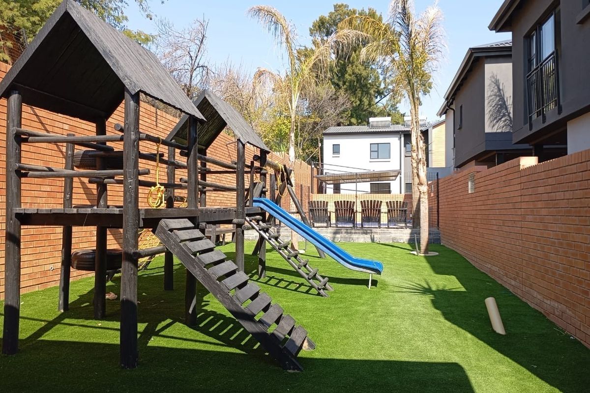 A well-maintained rear garden featuring a wooden jungle gym, artificial lawn, and high brick boundary walls for privacy.