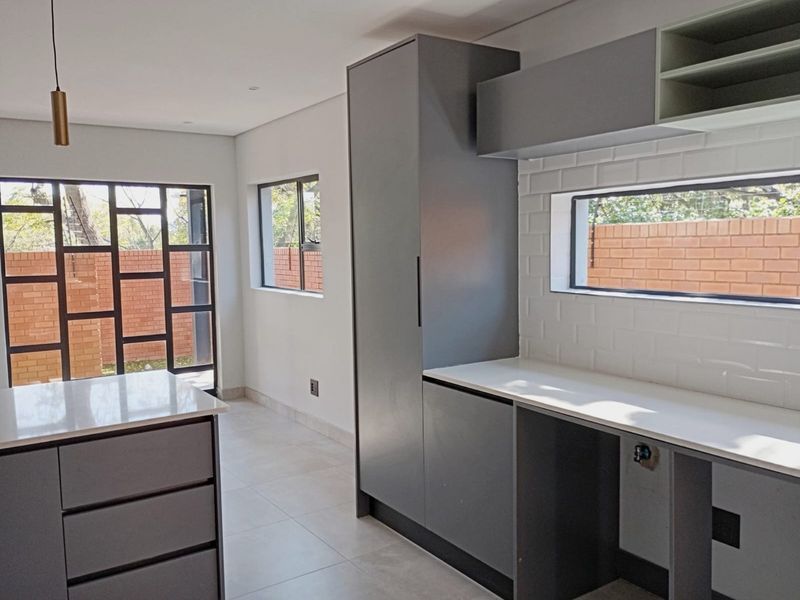 Modern kitchen featuring sleek grey cabinetry, white stone countertops, subway tile backsplash, and a central island, offering a clean and contemporary aesthetic.