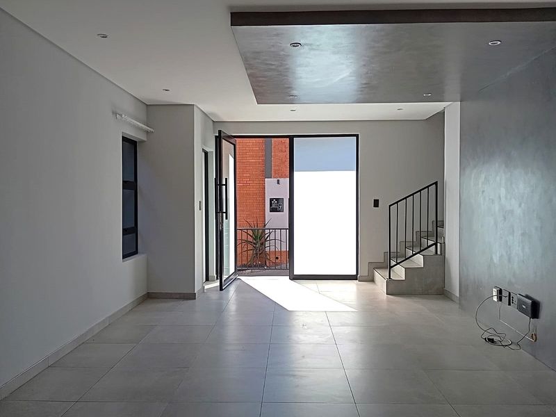 A bright, modern open-plan living area featuring large format floor tiles, a contemporary feature wall, and a staircase with a sleek metal balustrade.
