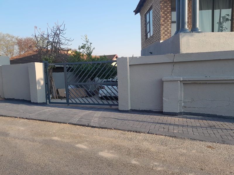 Front view of the property featuring a metal driveway gate and a boundary wall with visible structural cracking in the plaster.