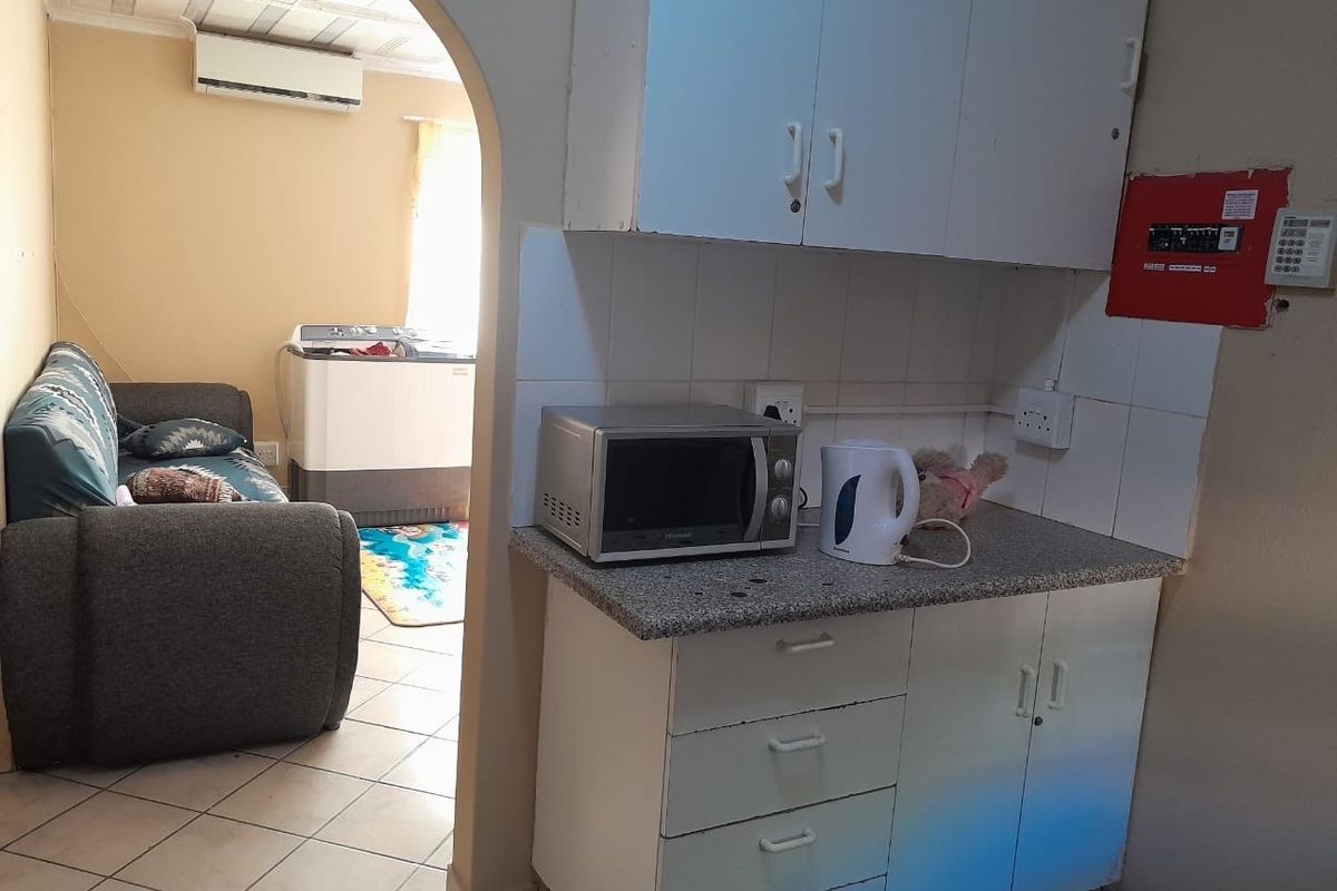 Compact kitchen area featuring built-in cabinetry and tiled splashback, with an adjacent living space visible through an arched doorway.