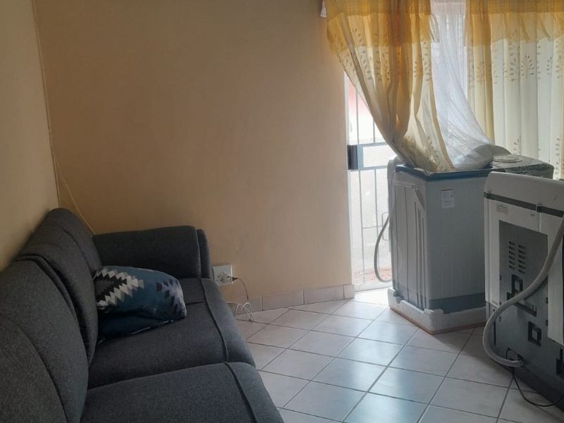 A living area featuring tiled flooring, a wall-mounted air conditioning unit, and access to an outdoor space through a sliding security door.