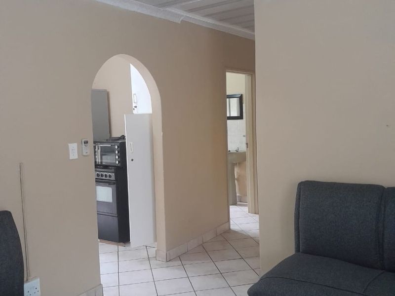 A living area featuring tiled flooring and an arched doorway leading to a kitchen, with a coved ceiling and neutral wall finishes.