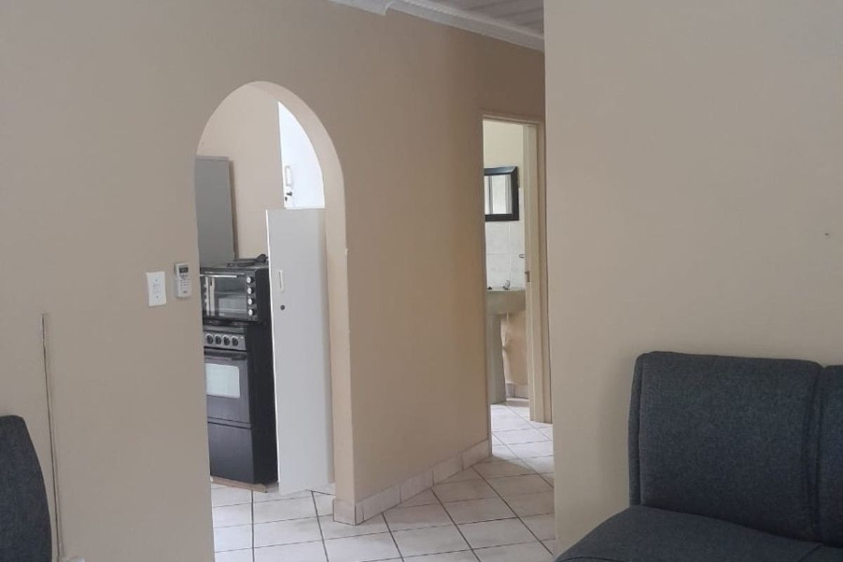 A living area featuring tiled flooring and an arched doorway leading to a kitchen, with a coved ceiling and neutral wall finishes.
