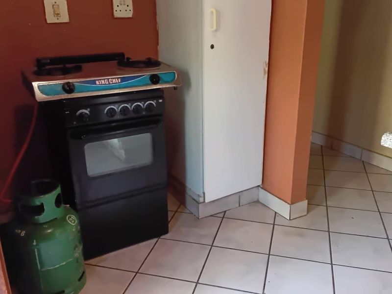 A compact kitchen area featuring tiled flooring and a freestanding gas stove setup against a painted wall.