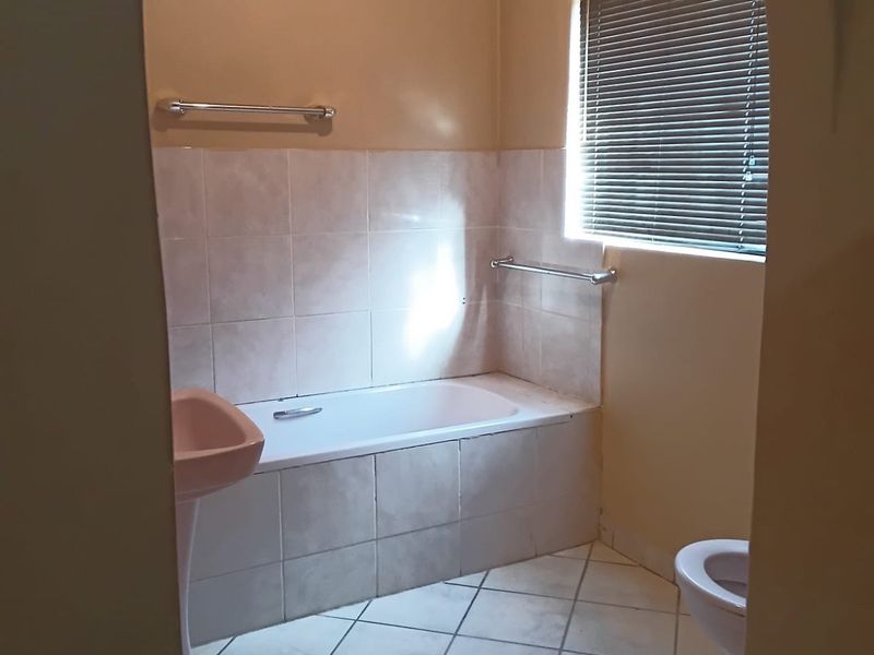 A dated bathroom featuring a pedestal basin, built-in bathtub, tiled flooring, and neutral wall finishes, offering potential for a modern renovation.