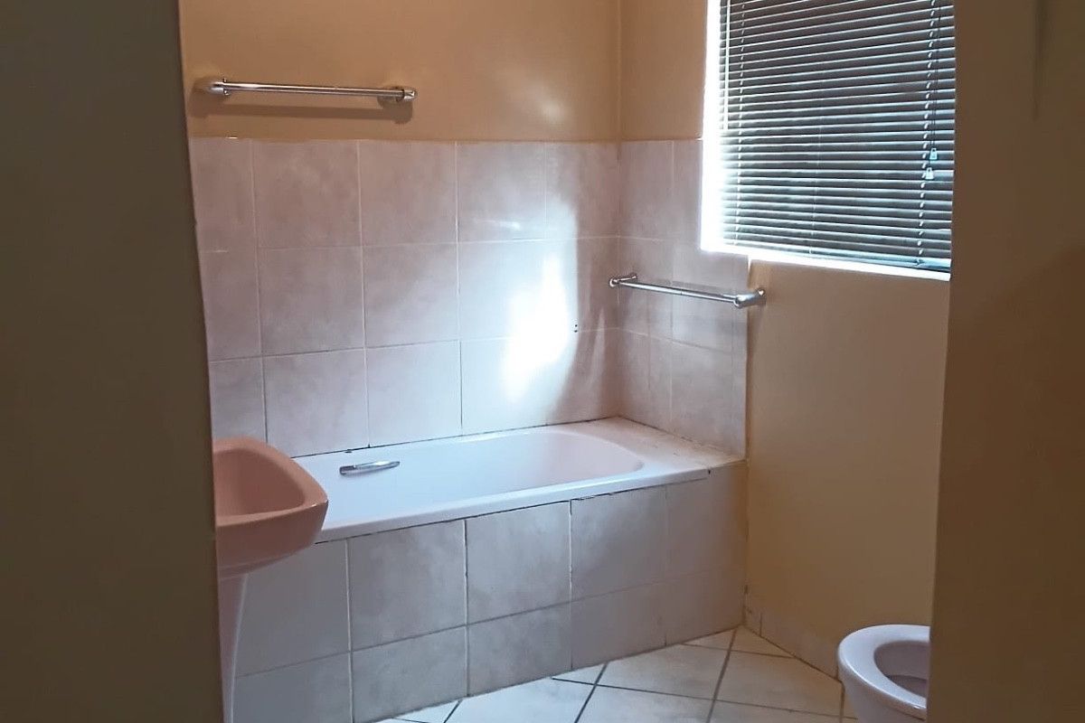 A dated bathroom featuring a pedestal basin, built-in bathtub, tiled flooring, and neutral wall finishes, offering potential for a modern renovation.