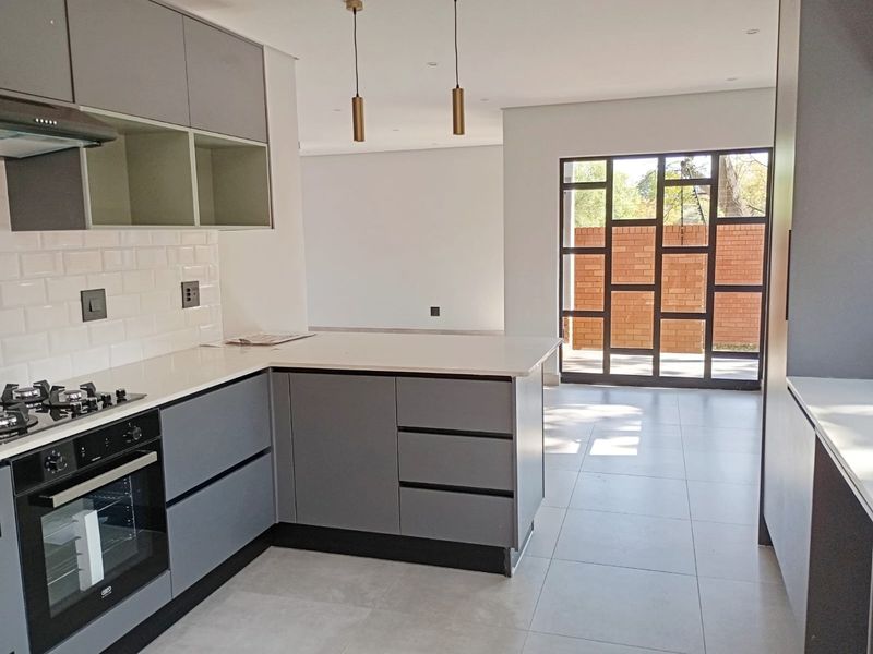 Modern open-plan kitchen featuring sleek grey cabinetry, stone countertops, integrated appliances, and a large glass door leading to an outdoor area.