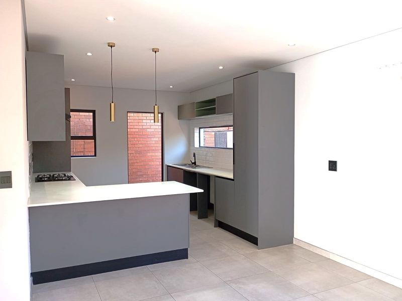 Modern kitchen featuring sleek grey cabinetry, stone countertops, a gas hob, and tiled flooring in a clean, contemporary open-plan layout.