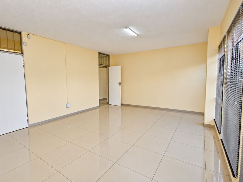 A bright, vacant office space featuring neutral tiled flooring, large windows with venetian blinds, and clean, well-maintained walls.